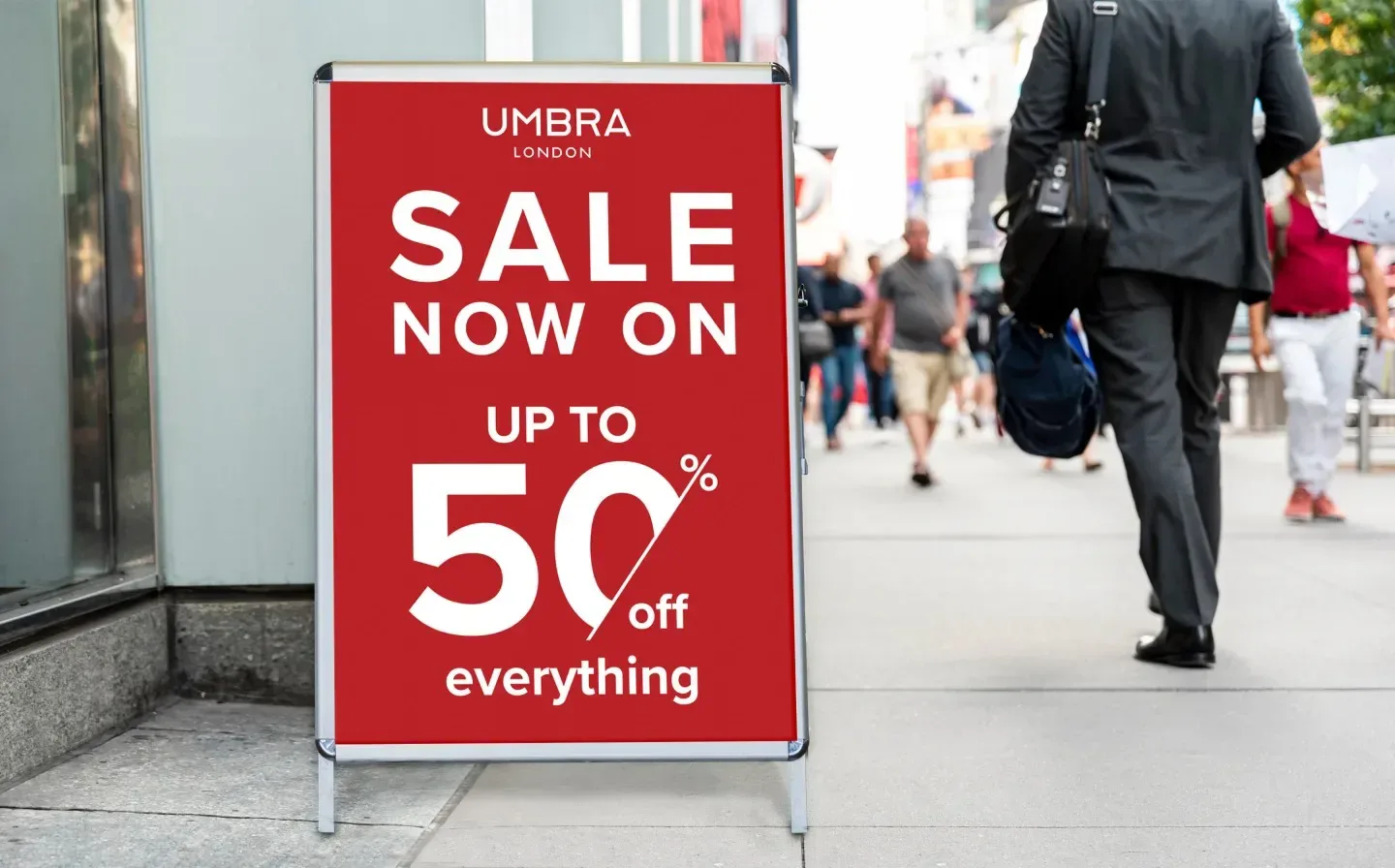 A man strolls down the street, passing an a frame sign advertising a sale