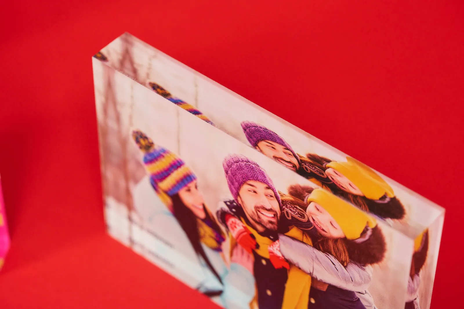 printed acrylic block with picture of a mother father and daughter playing in the snow with wooly hats and jackets on a bright red background