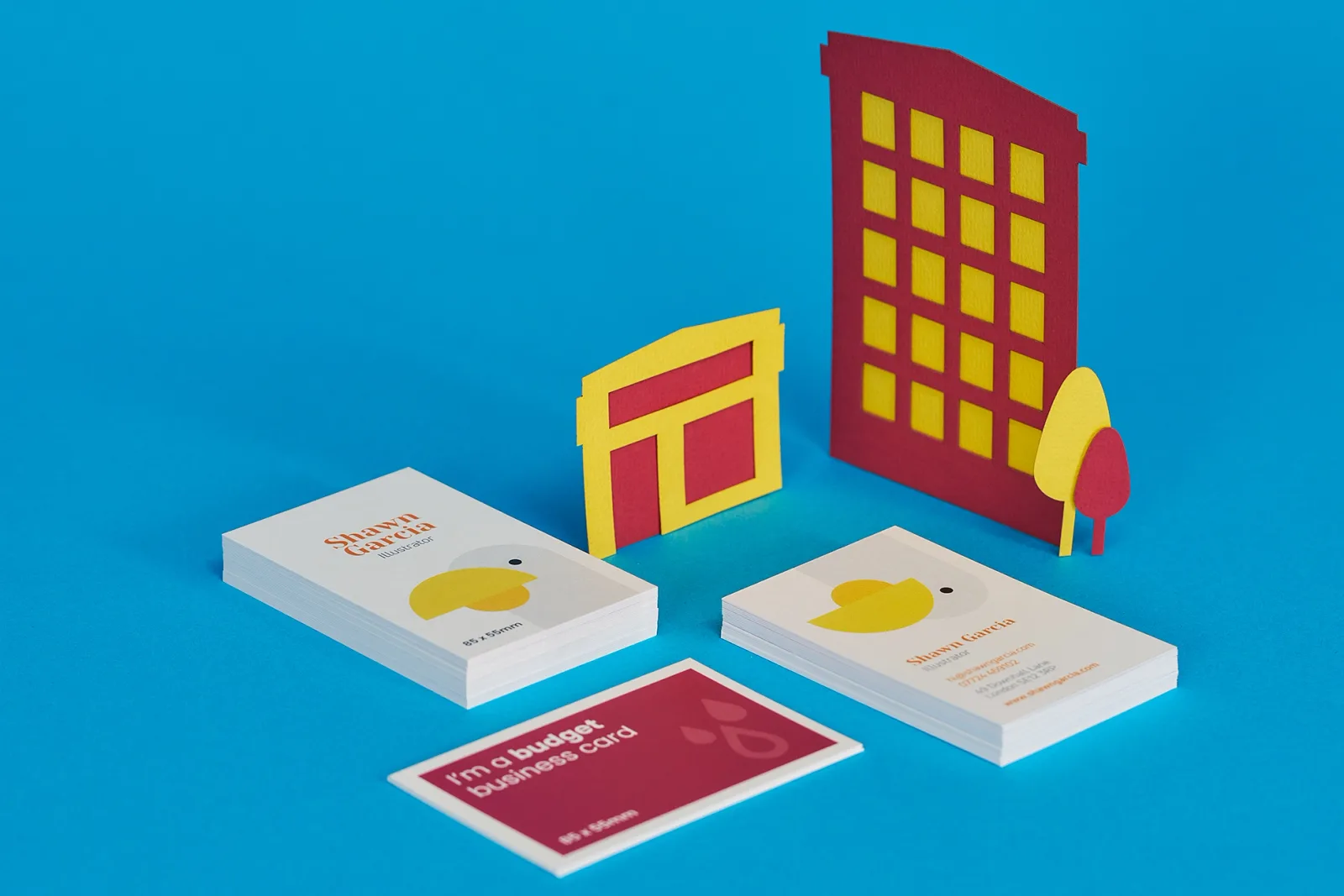 3 piles of 85 x 55mm business cards portrait and landscape, one printed purple with text 'im a budget business card' and the others printed with a bird with yellow beak with text 'shawn garc
