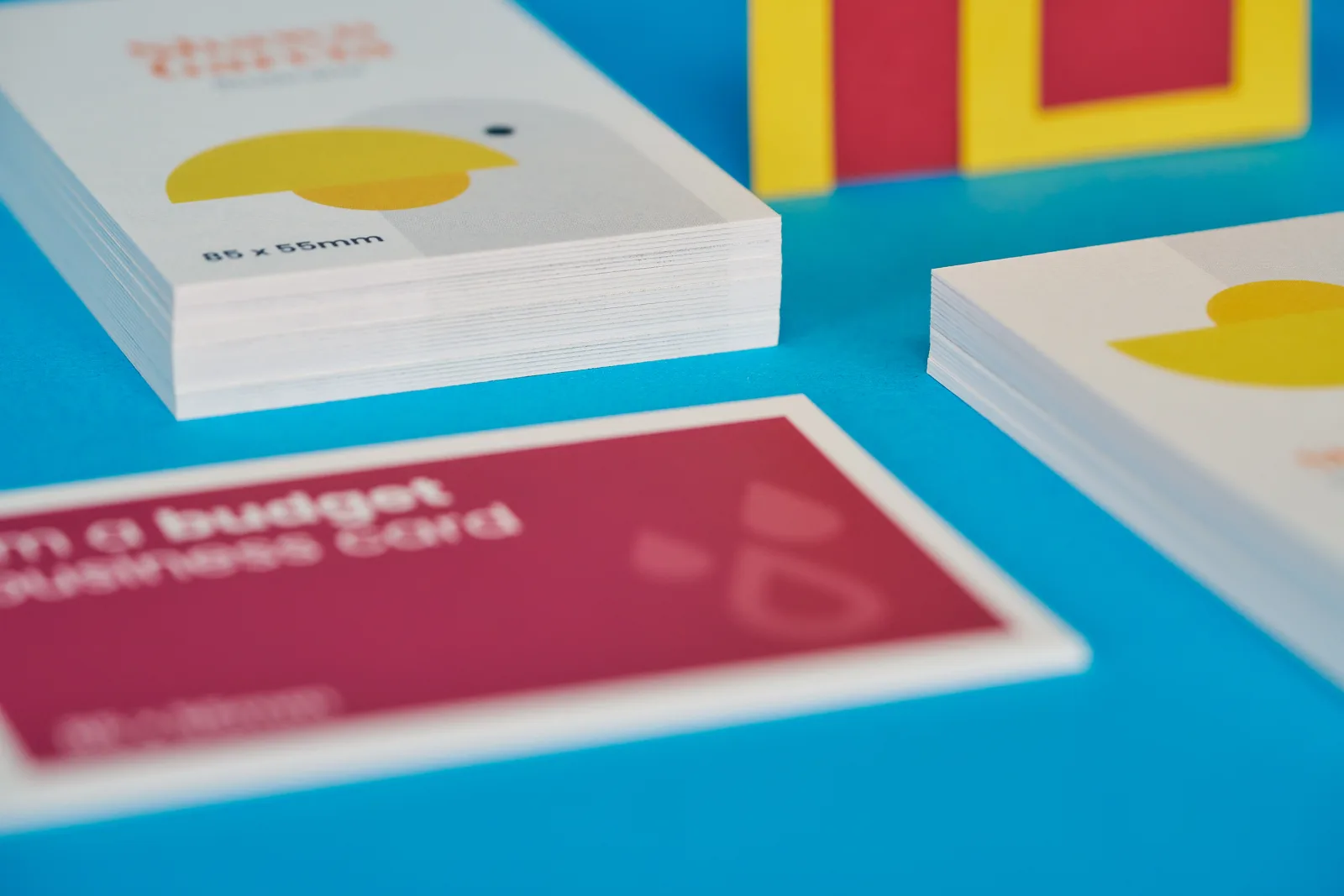 close up 3 piles of 85 x 55mm business cards portrait and landscape, one printed purple with text 'im a budget business card' and the others printed with a bird with yellow beak on a bright 