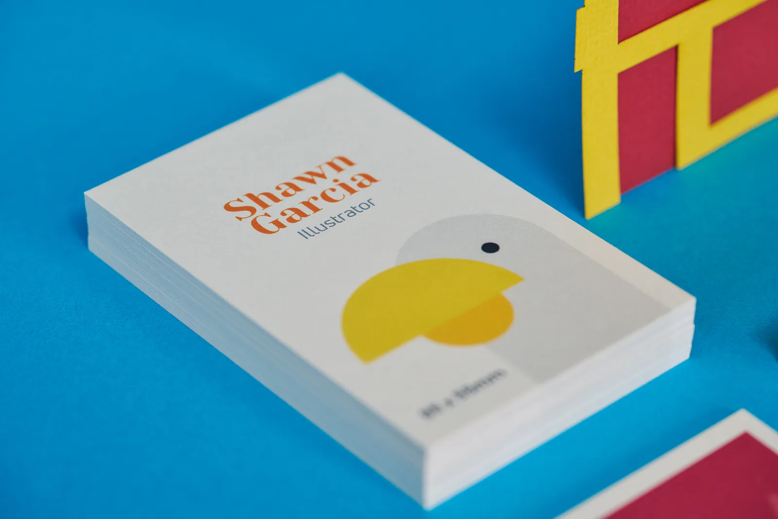 pile of white 85 x 55mm portrait business cards with a bird with yellow beak and the text 'shawn garcia illustrator' on a bright blue background