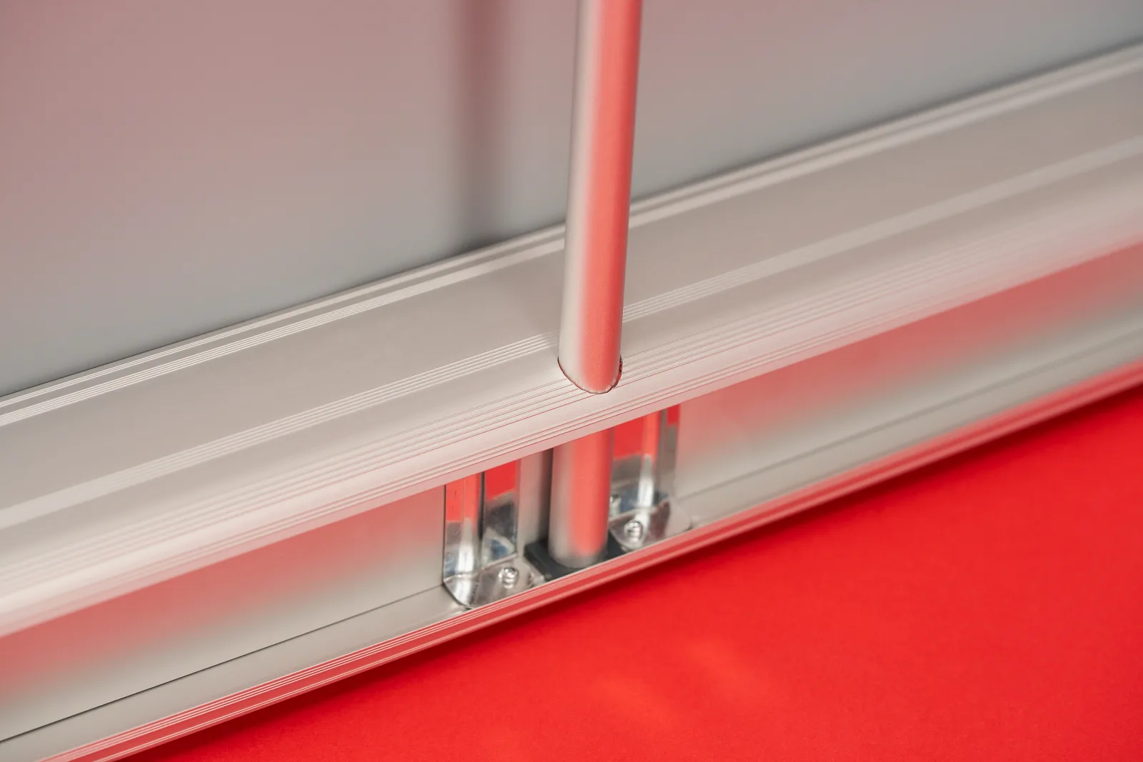 rear close up detail of a silver classic roller banner cassette showing the support pole connected to the cassette on a bright red background