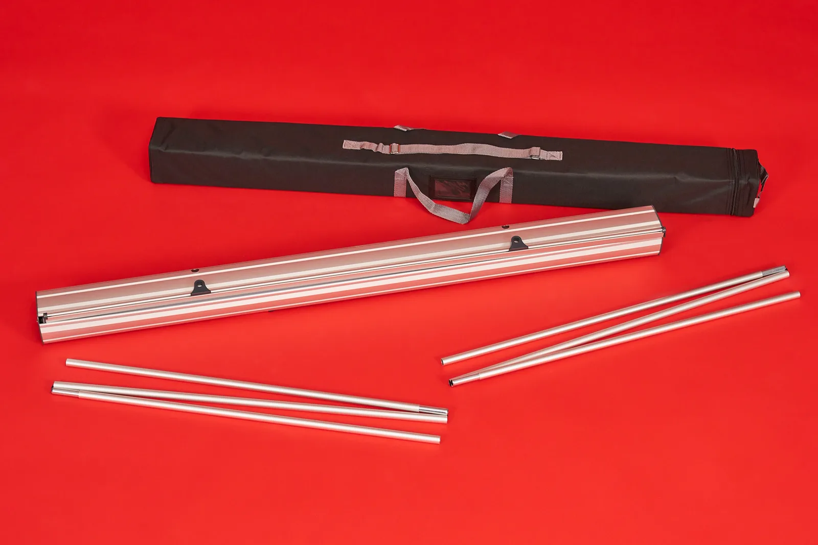 components of a classic roller banner including carry bag, silver cassette and 2 support poles on a bright red background