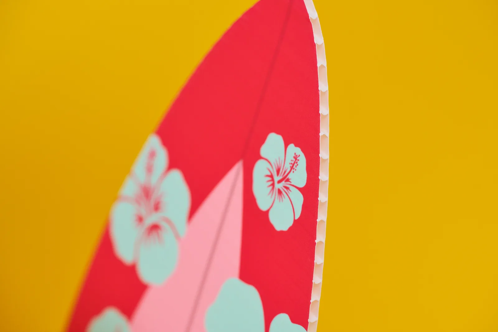 close up of a surfboard shaped correx© board printed red and pink with light blue flowers on a bright yellow background