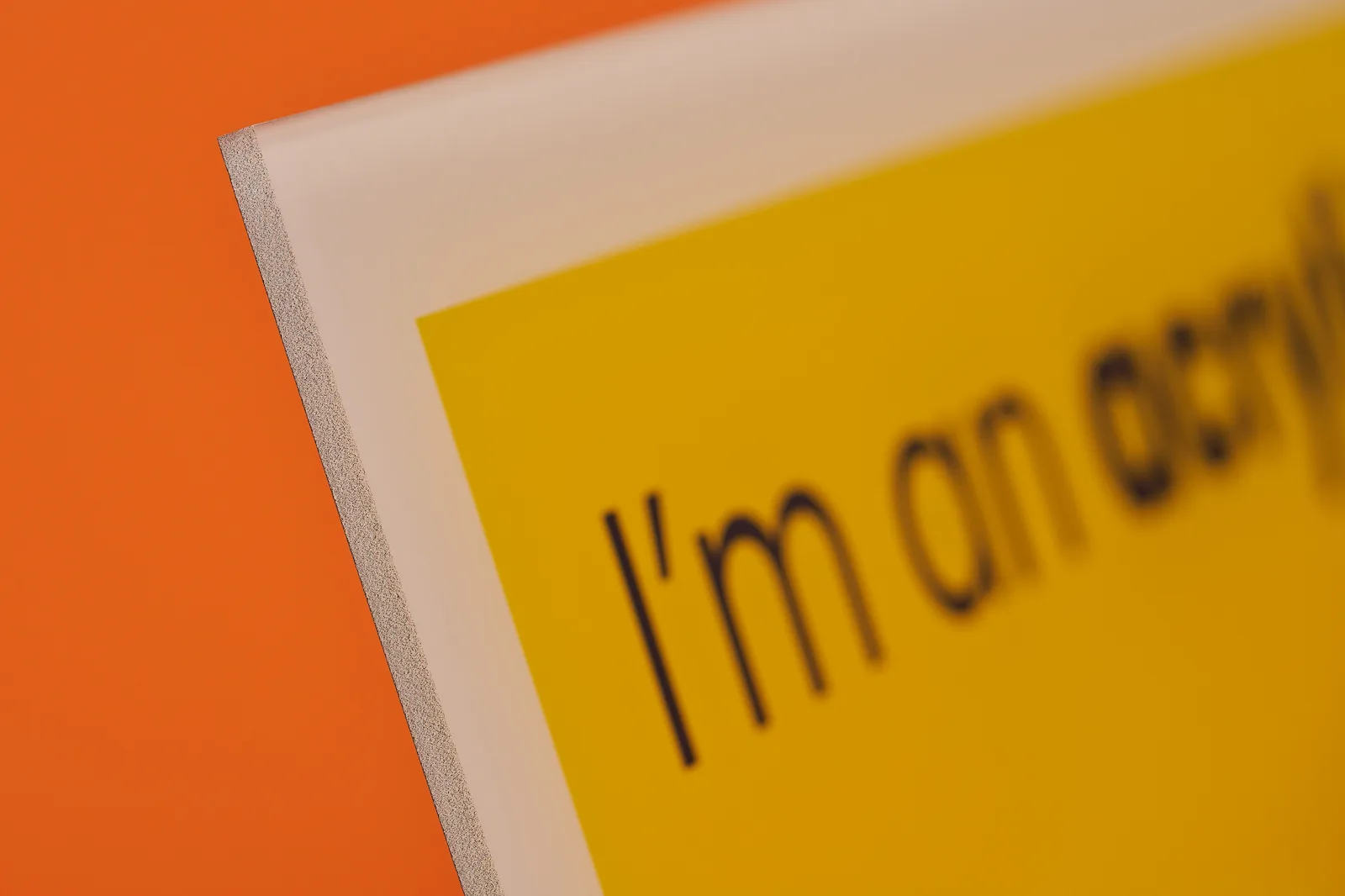 close up of the corner of a yellow and white acrylic print with text 'i'm an acrylic' on a bright orange background