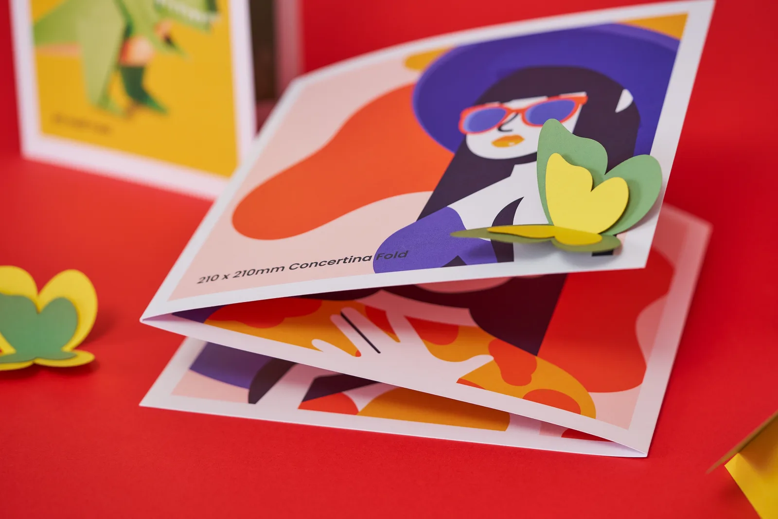 Close up of a 210 x 210mm 210 x 210mm concertina leaflet with blue illustration of a lady in sunglasses and hat on a bright red background with 2 yellow and green paper butterflies