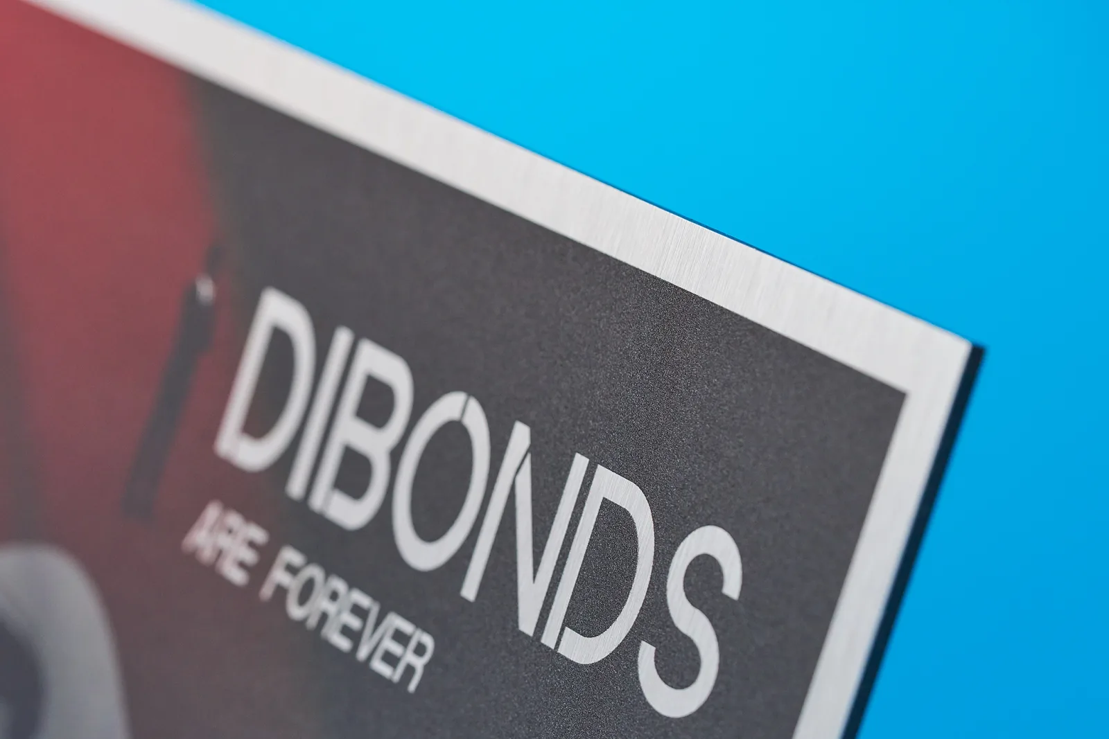 Close up of a brushed aluminium dibond sign with red and black print with wording 'dibonds are forever' on a bright blue background