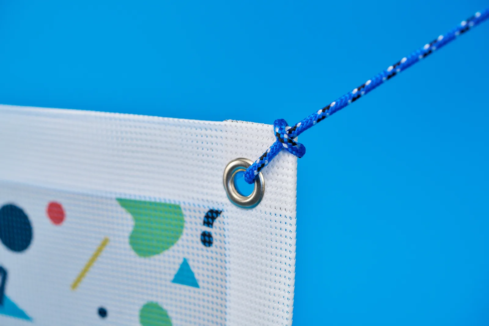 close up of a outdoor fence mesh banner showing eyelet, rope and detail of mesh on a bright blue background