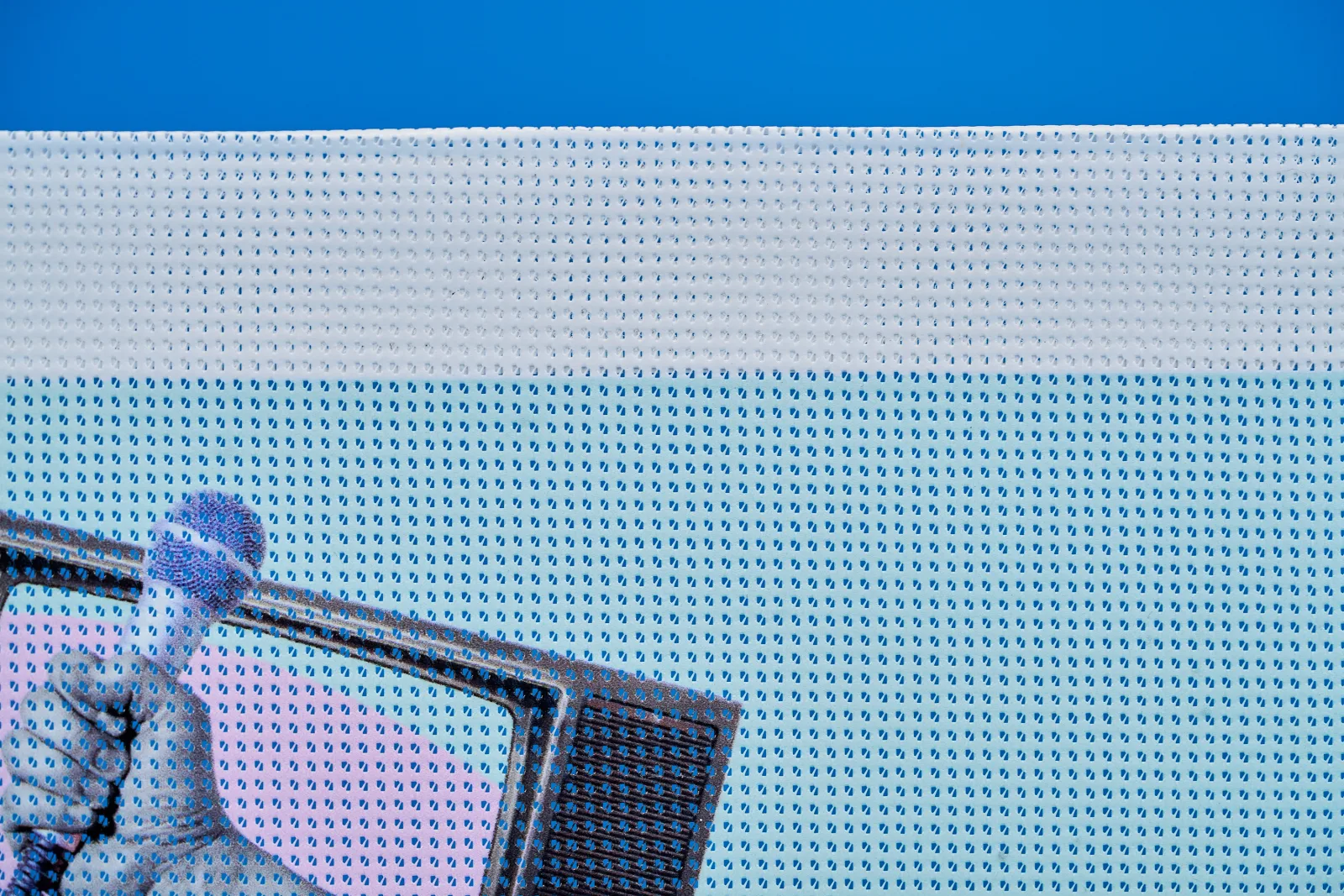 close up detail of a printed outdoor mesh fence banner on bright blue background