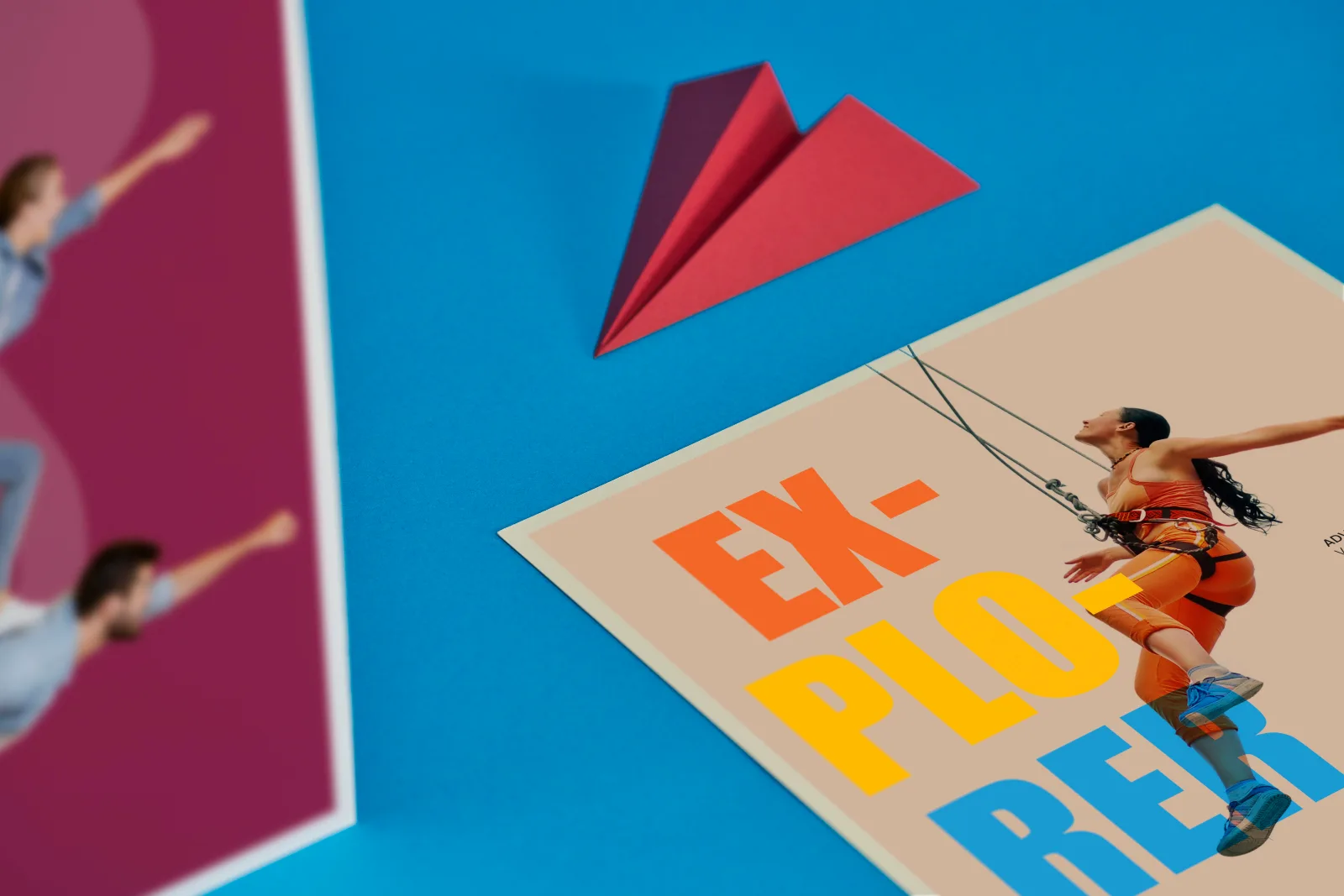 Close up of printed flyers, purple A4 portrait and a 210 x 210mm with word 'explorer' and a lady abseiling in orange clothes on a bright blue background