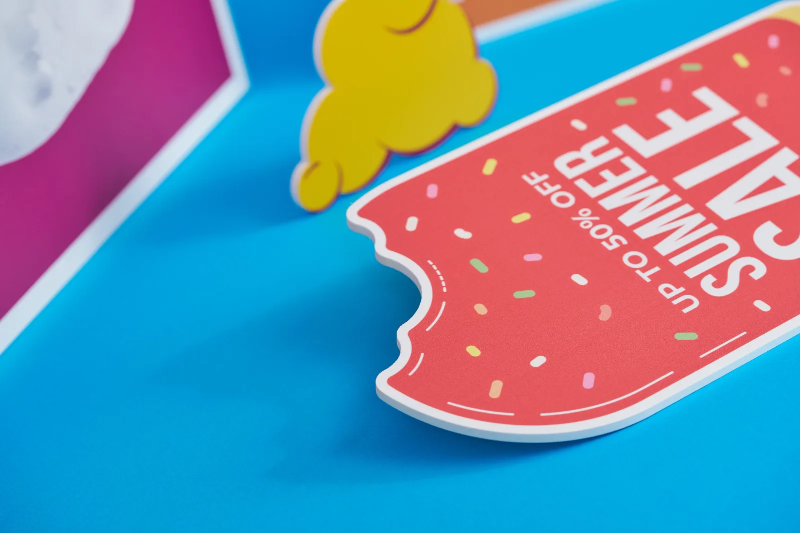Close up of a red foamex lollipop shape sign with cutout teeth marks with wording 'up to 50% off summer sale'. Yellow foamex soap bubbles on a bright blue background