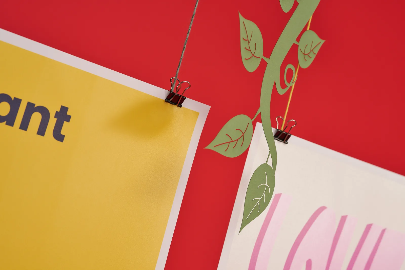 Close up of 2 giant posters one yellow on one cream hanging from string and bulldog clips on a bright red background with green paper beanstalk