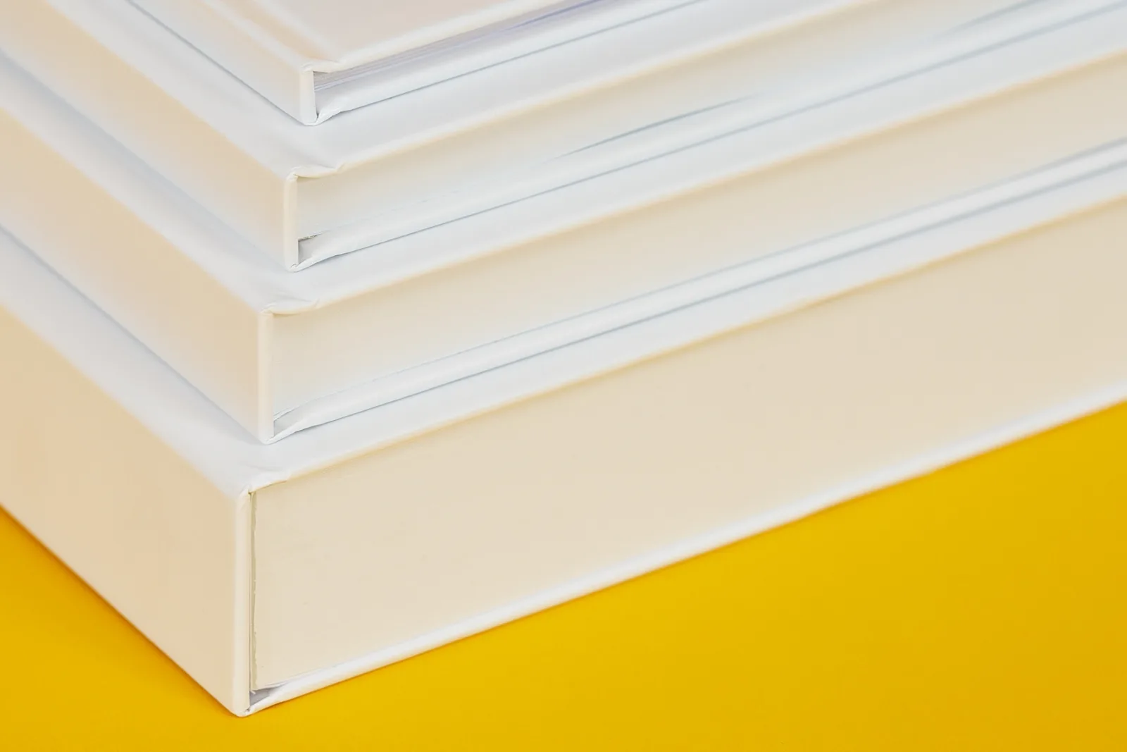 close up detail showing different spine thicknesses of 4 printed hardback books on a bright yellow background