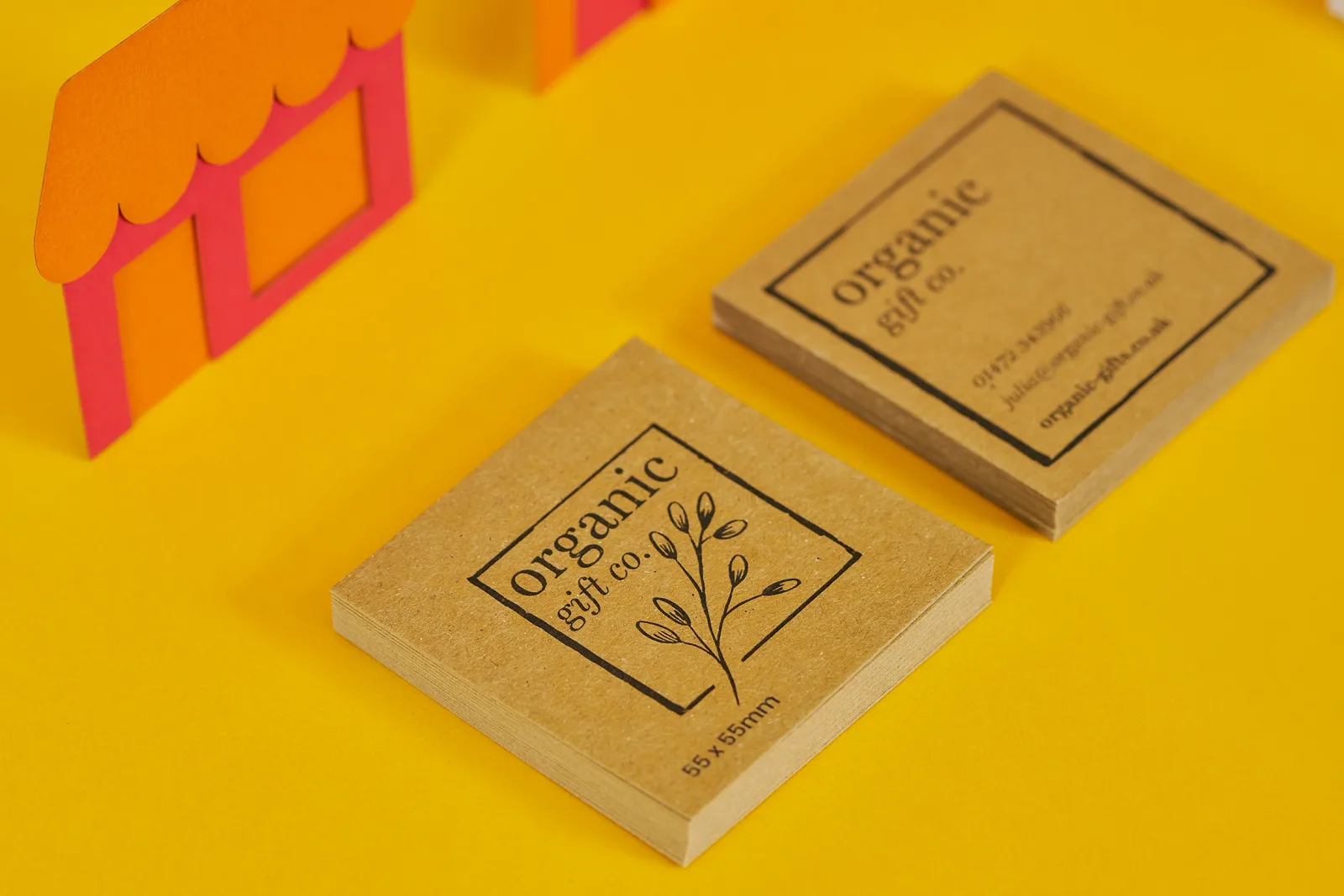 kraft business cards with black print text 'organic gift co' on bright yellow background with orange and red paper building