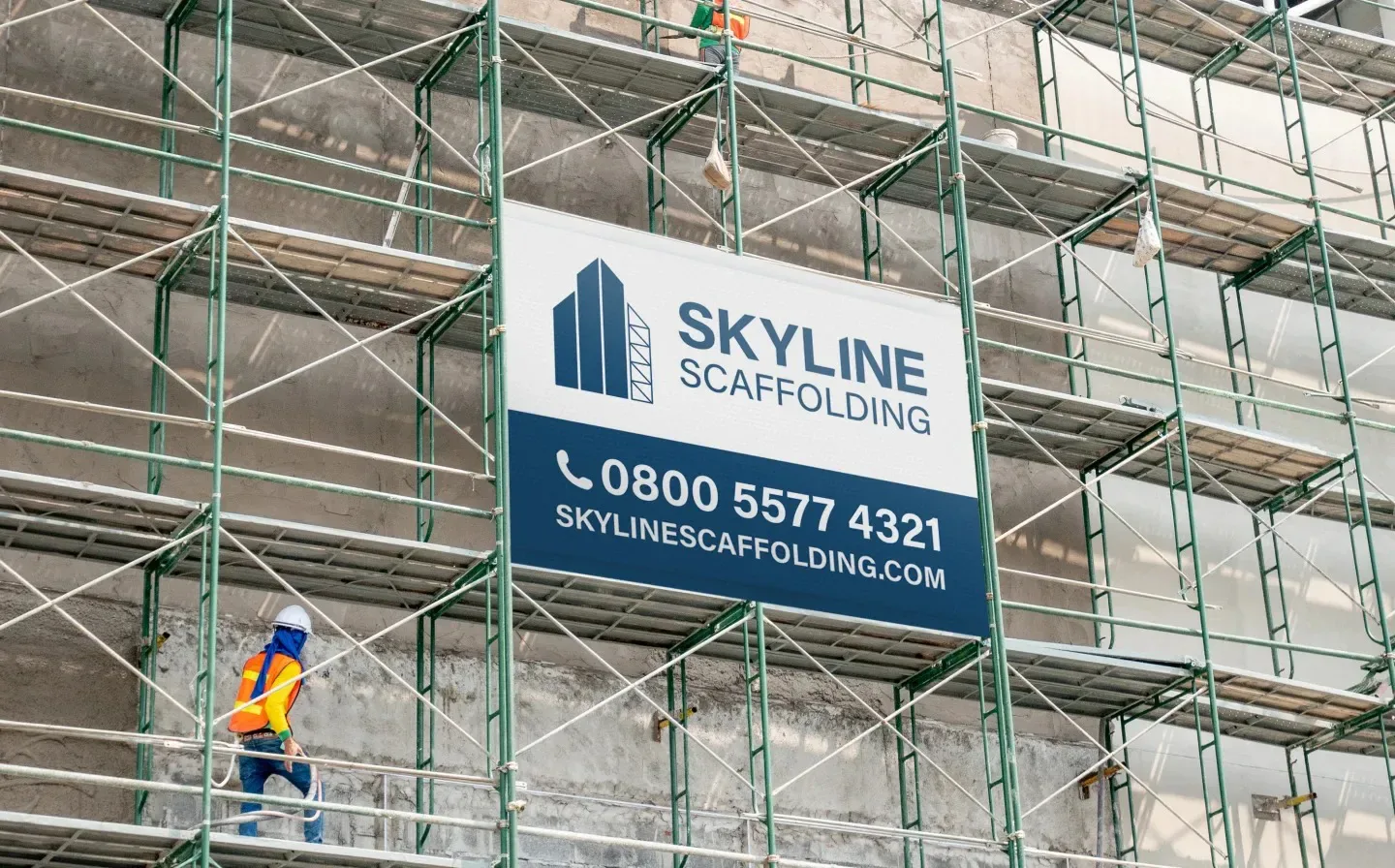 A construction worker on-site at the Skyline Building, with a pole pocket banner advertising the service