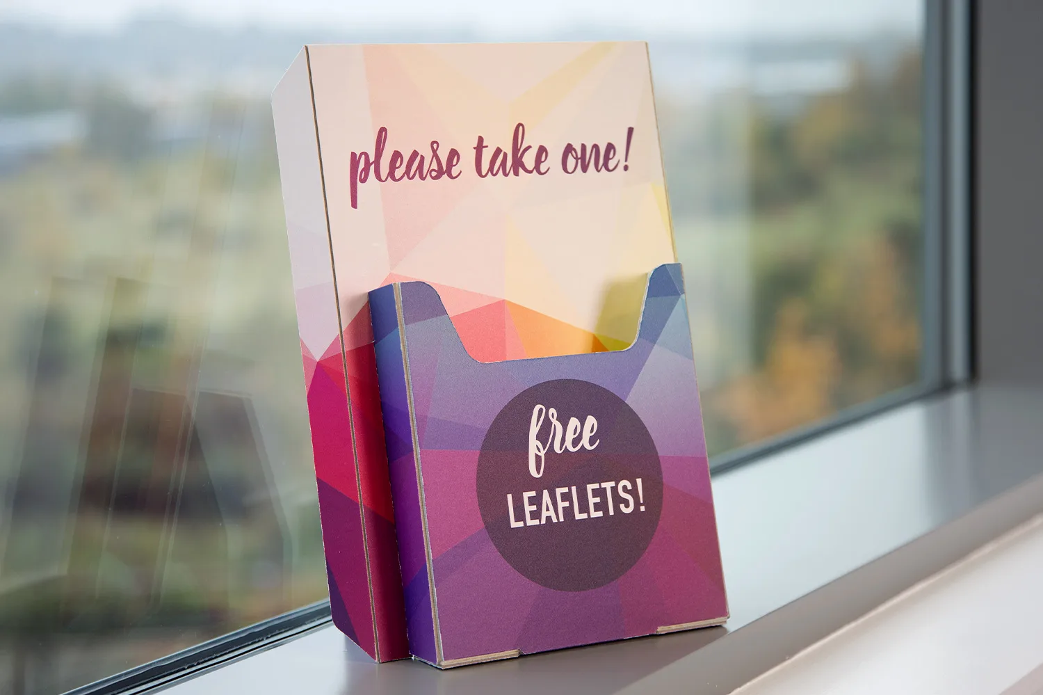 Cardboard display on windowsill with "please take one!" and "free leaflets!" text.