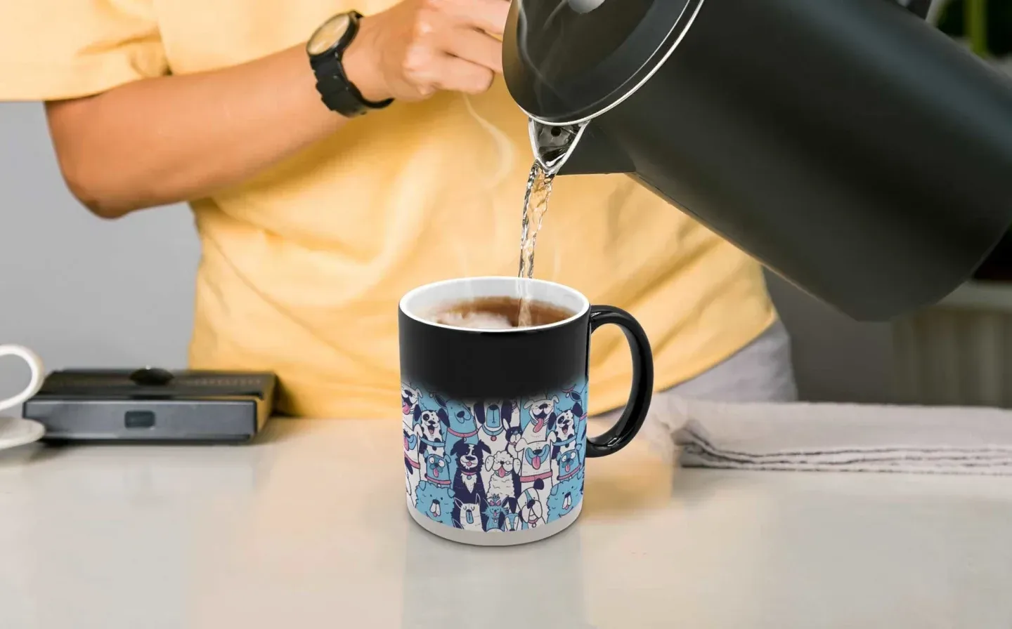 A man pours hot water from a kettle into a magic mug, showing a quirky dog design