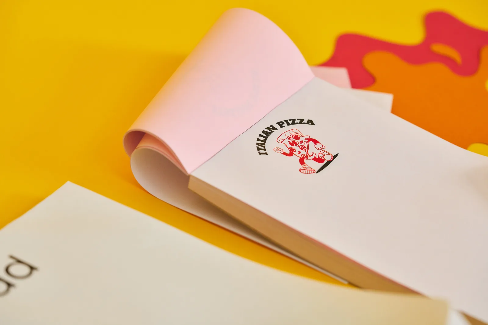 a6 ncr pad with red pizza logo and text 'italian pizza' with pink duplicate sheet on a bright yellow background with red and orange paper ink splats