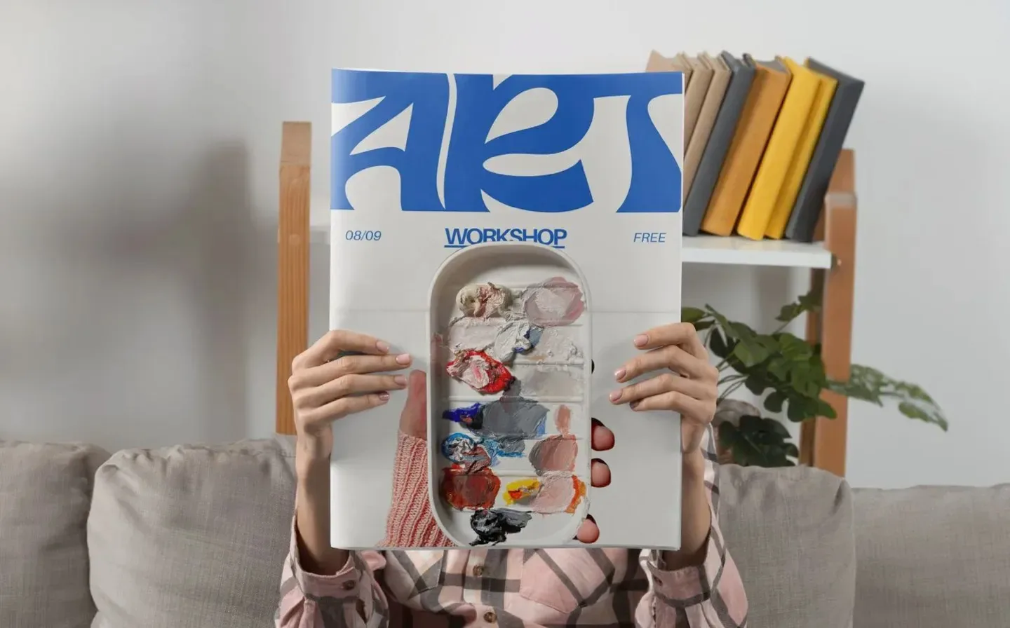 A person holding a newspaper with 'Art Workshop' in bold, blue lettering