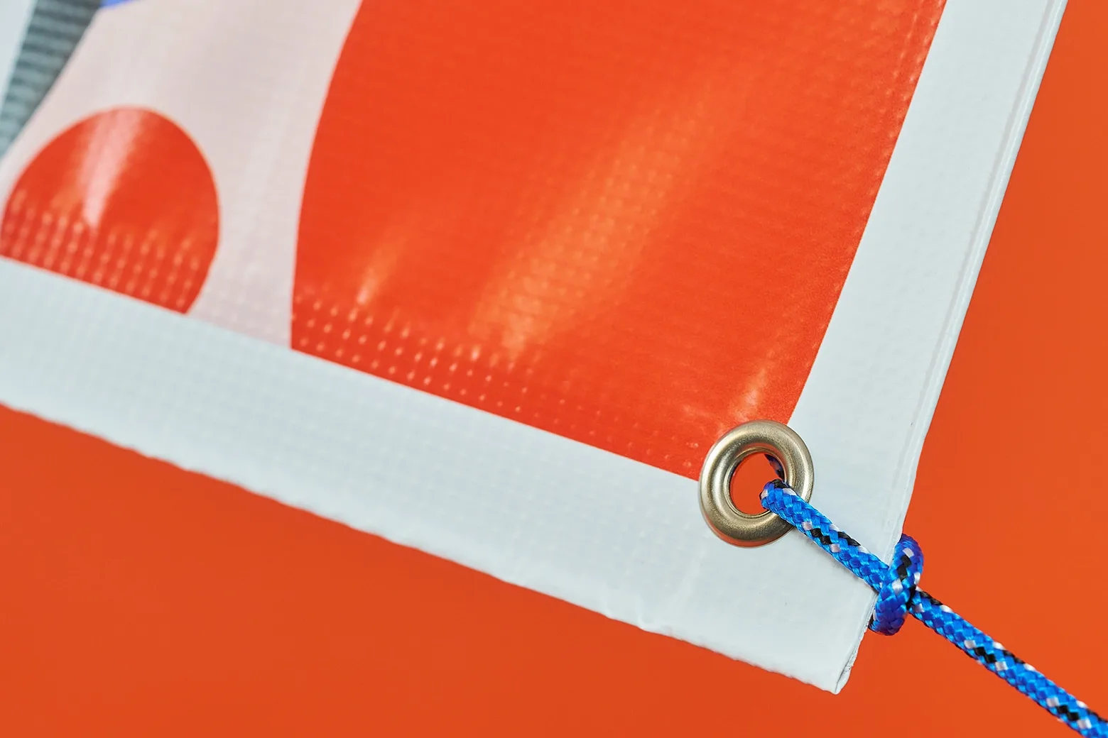 red and white printed outdoor pvc banner with eyelet and blue rope on a bright orange background