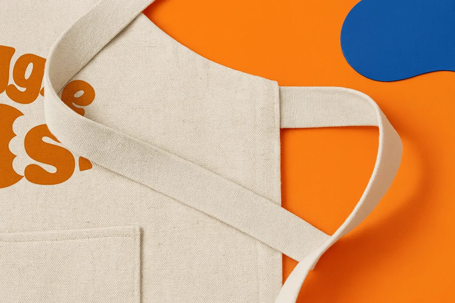 Beige canvas apron with a visible pocket, on an orange background with a blue shape.