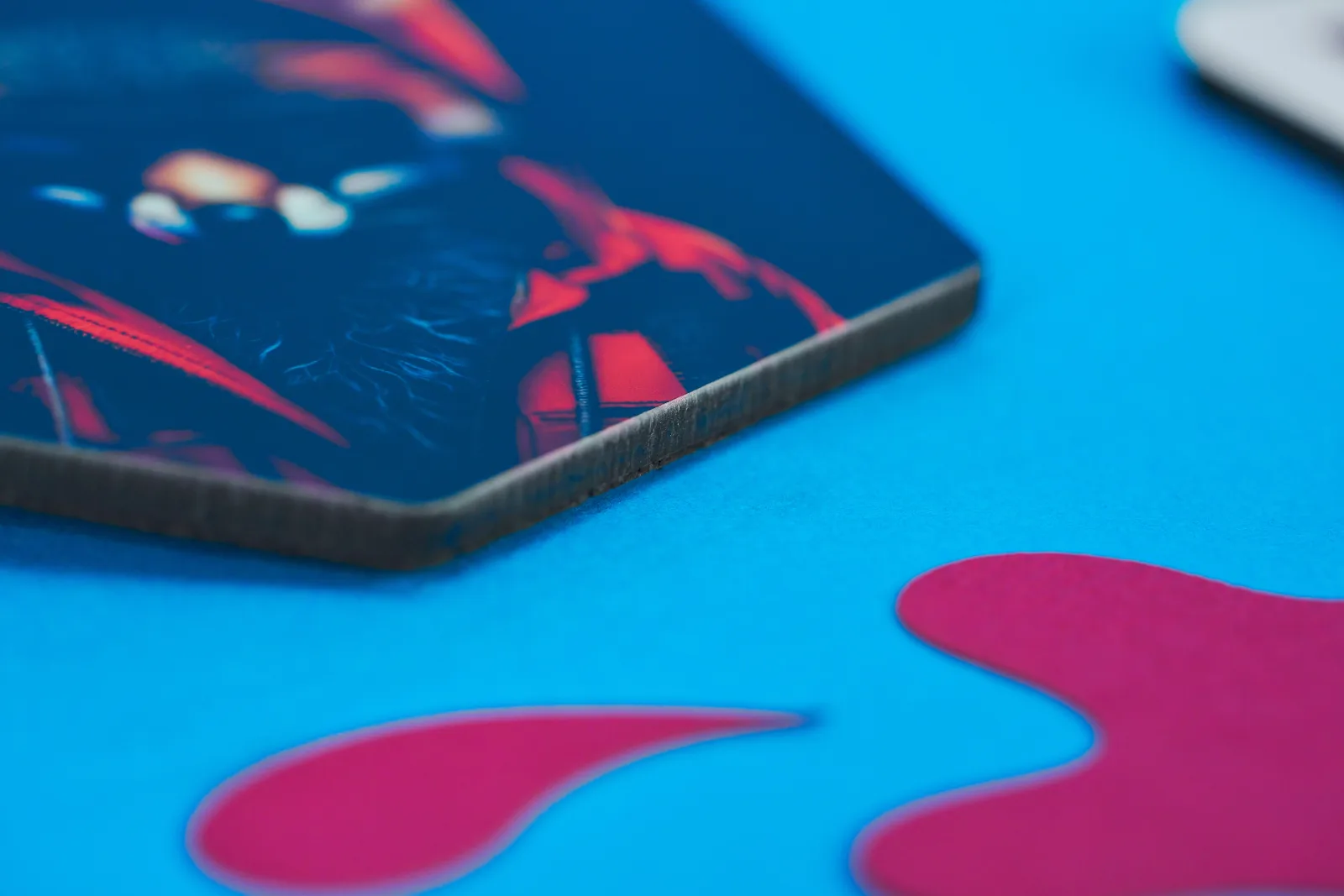 close up of the side of a hexagon printed coaster showing black edge and fox print on the top on a bright blue background with purple paper ink splats