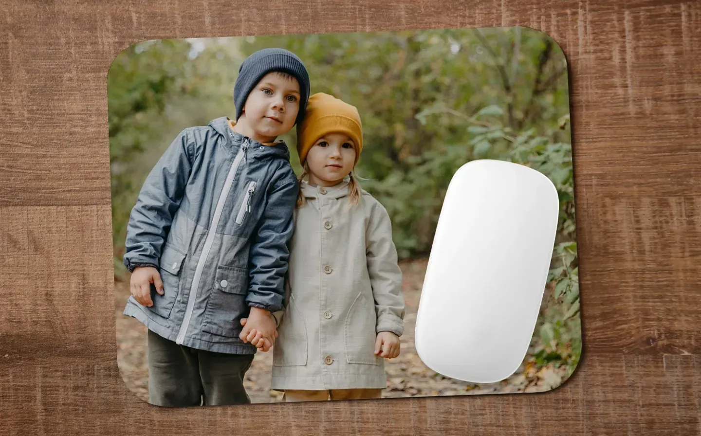 A mouse mat displayed on a wooden table featuring two children stand together in a forest 