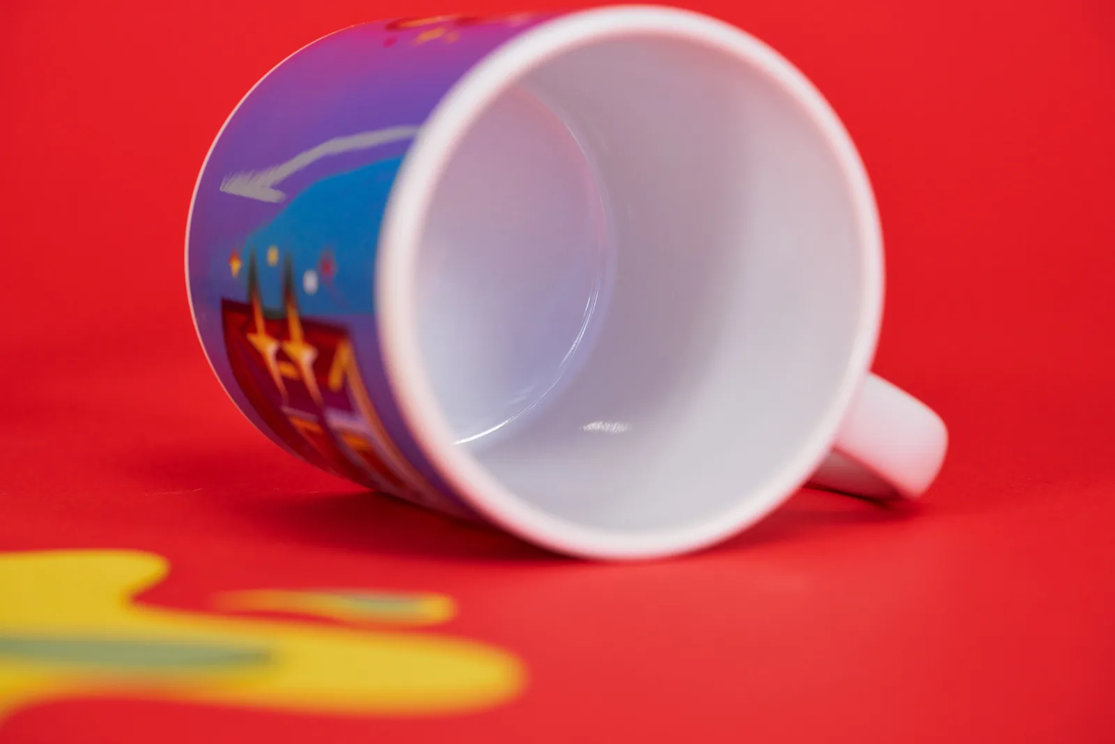 white mug laying on it's side showing the inside with blue print on the outside on a bright red background