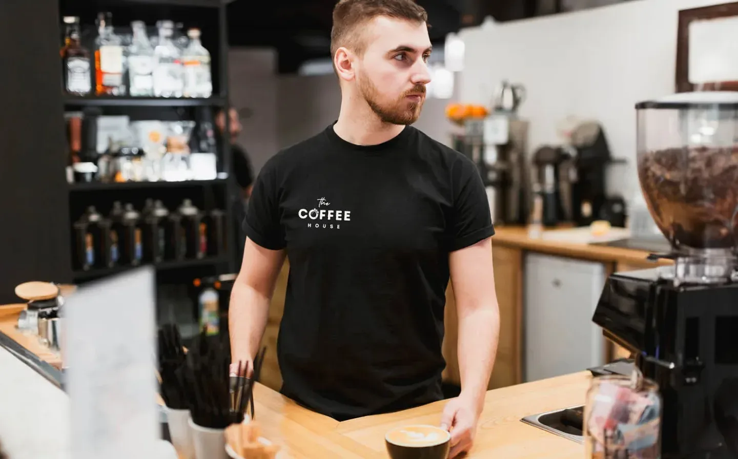 A man in a black logo t-shirt is positioned behind a counter, ready to assist or serve customers