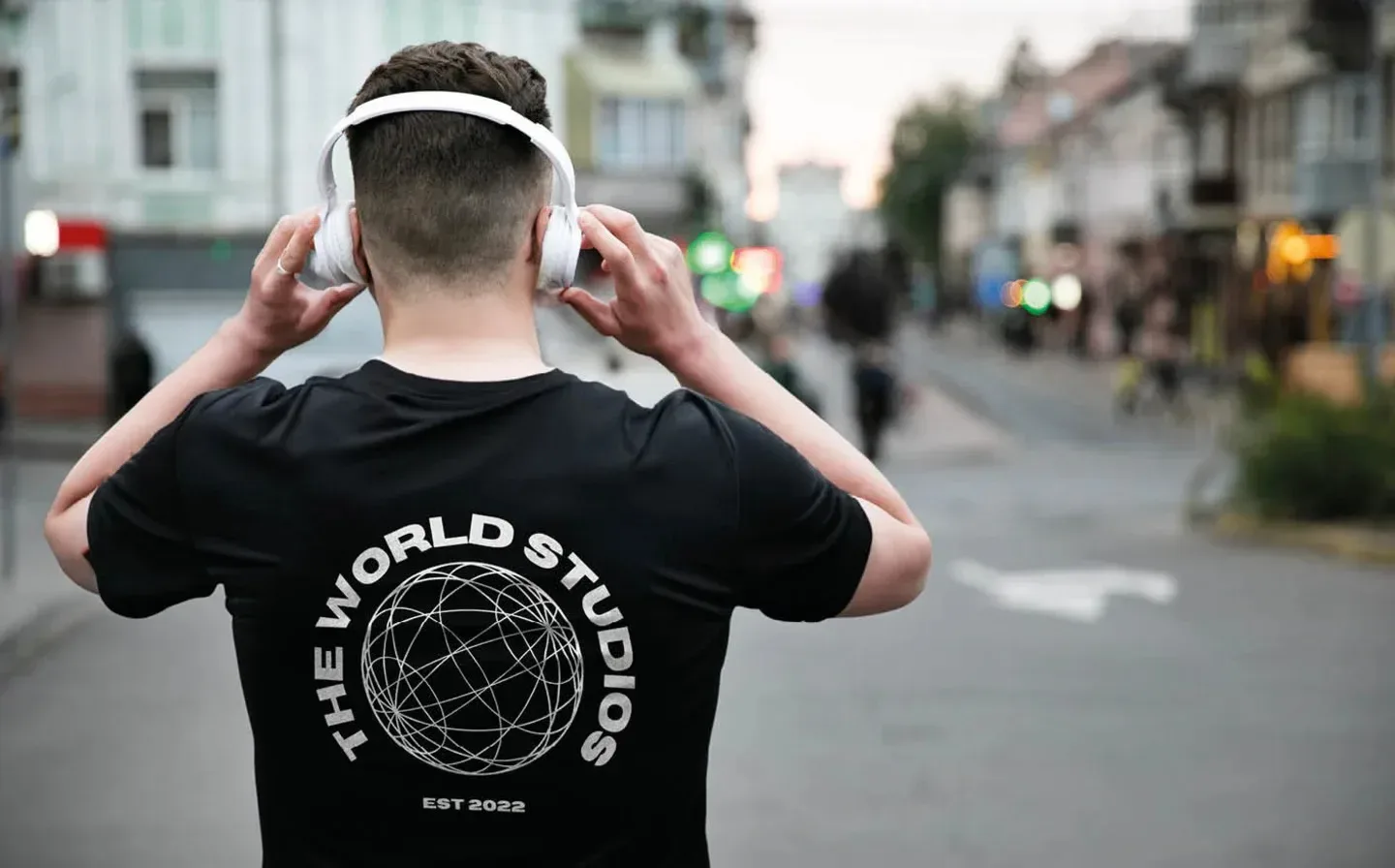 A man in headphones wears a black organic t-shirt featuring the words "the world studios" prominently displayed