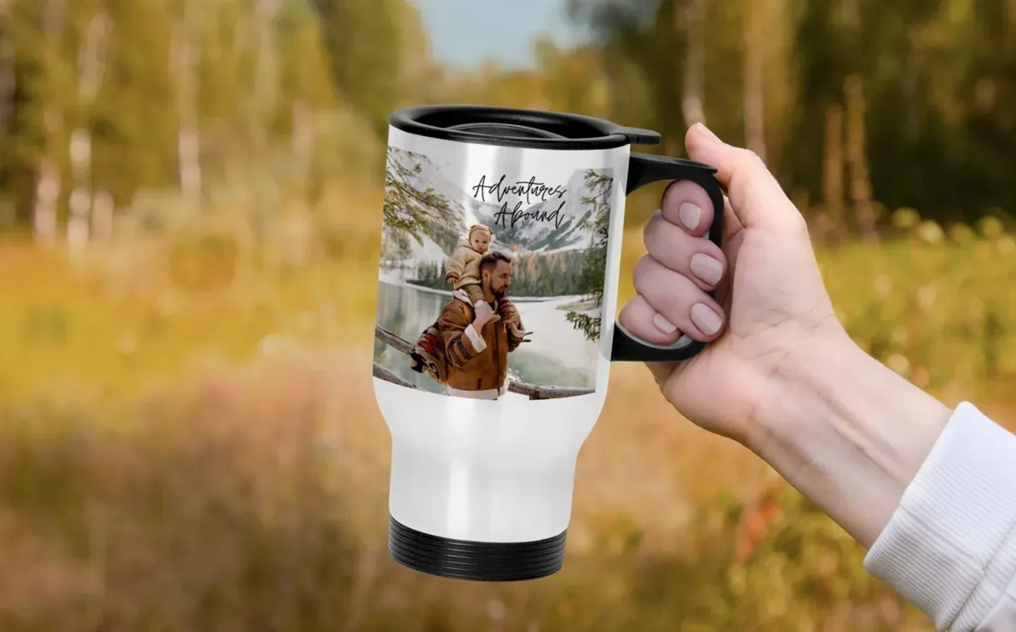 A hand holding a travel mug featuring a father and daughter, displayed on an outdoors backdrop