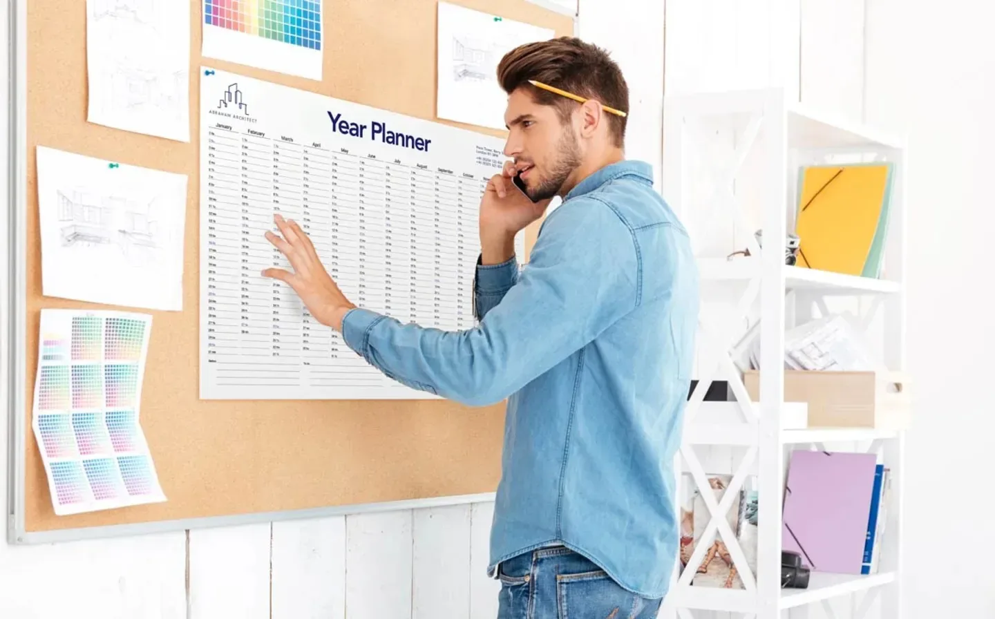 A man stands in front of a wall planner bulletin board, reviewing important dates and events displayed