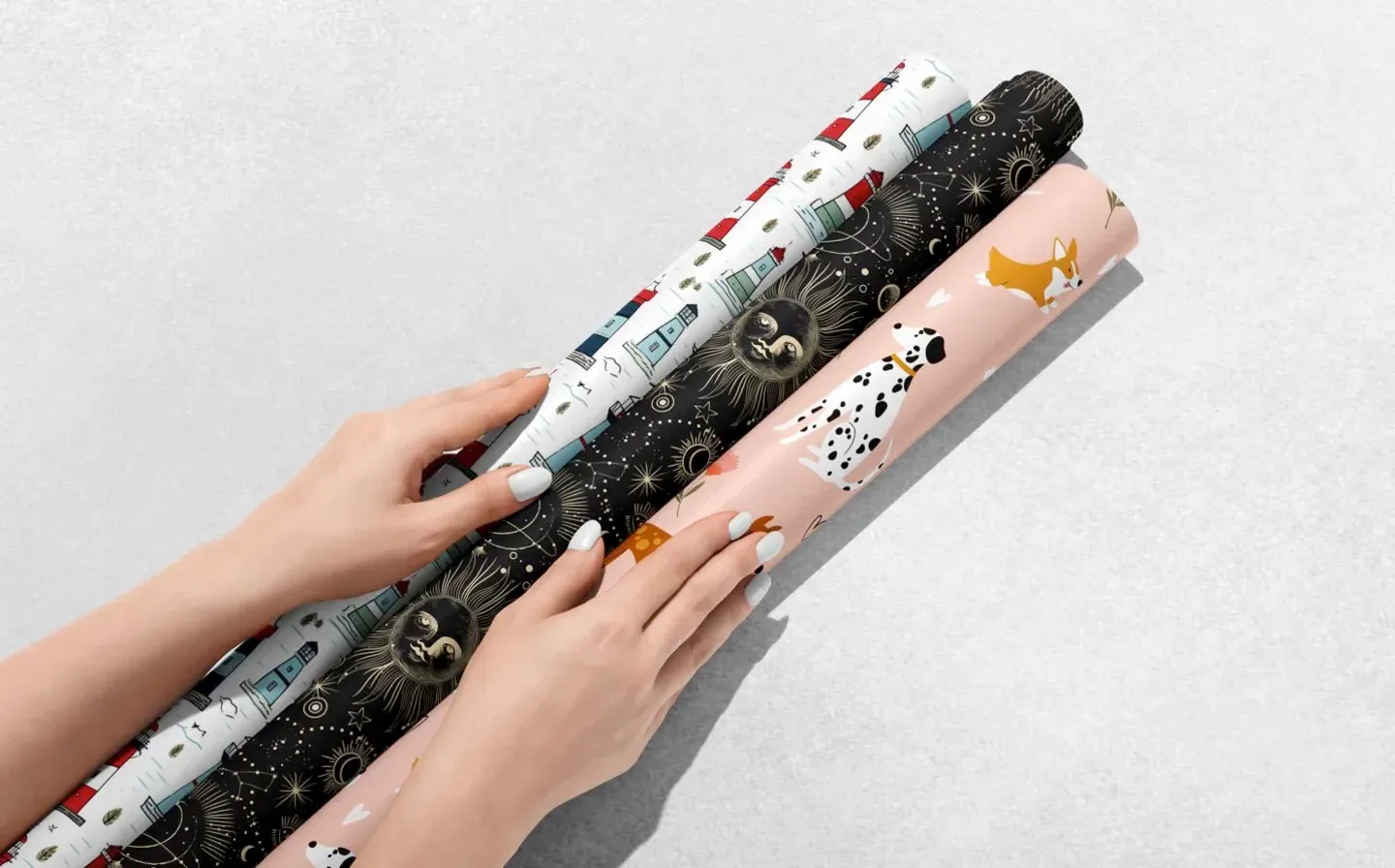 A woman holds three wrapping paper rolls featuring various bold designs on a plain background