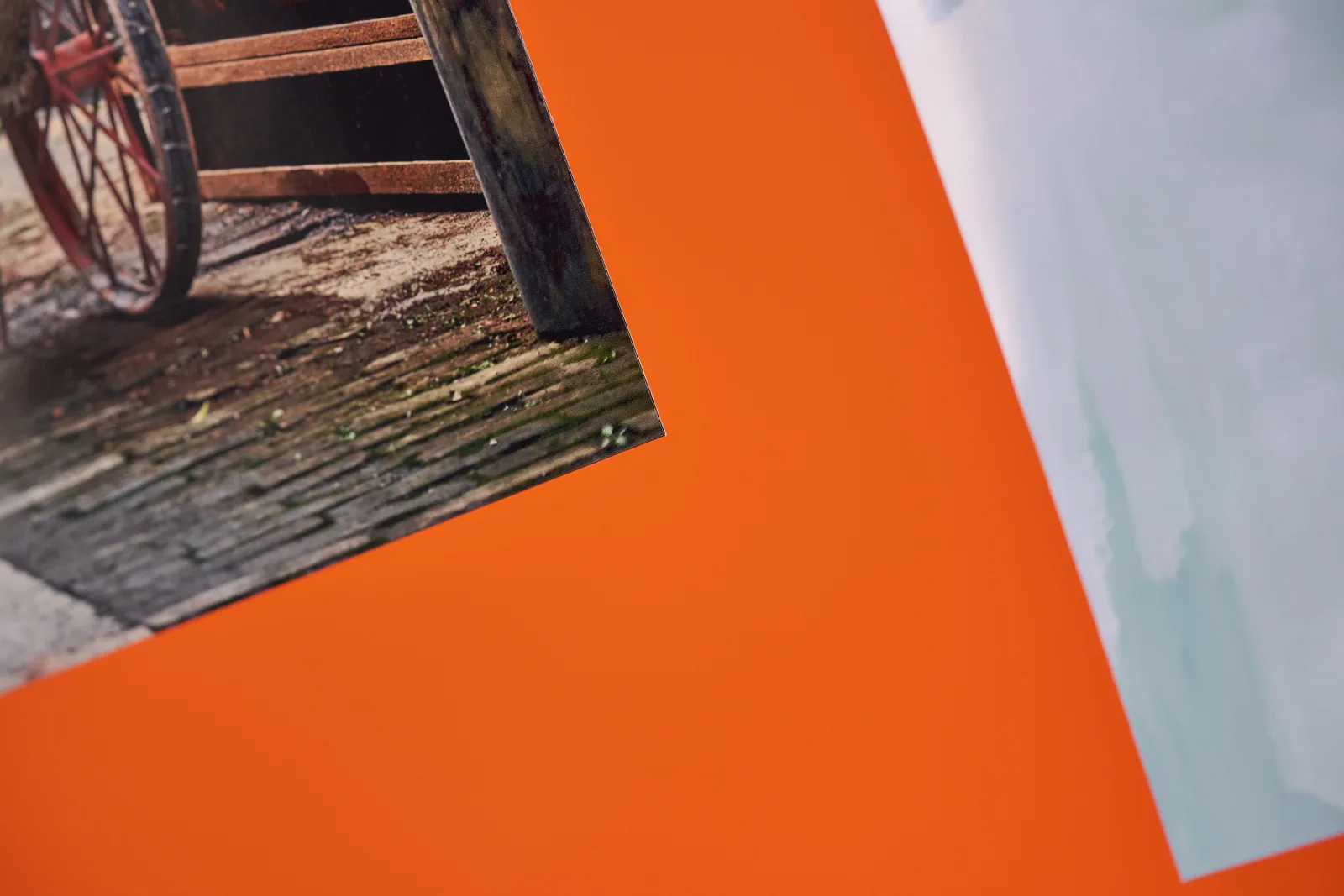 corner detail of a photo poster of a cobbled street with red wheel on a bright orange background