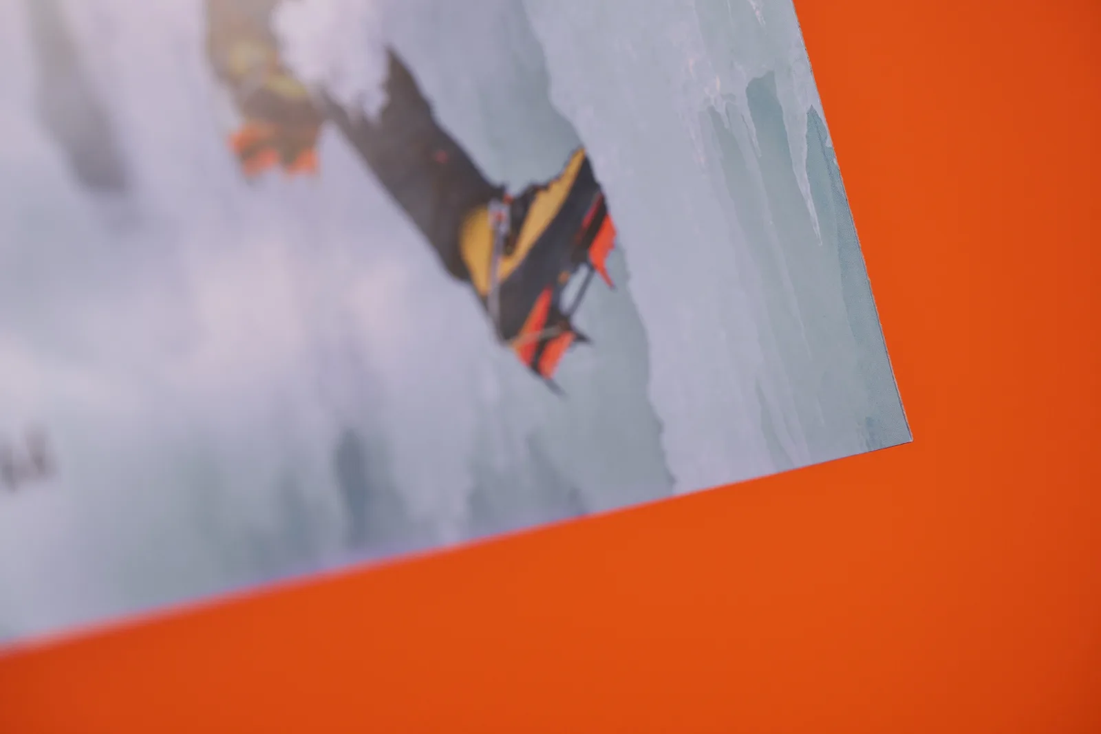 corner detail of a photo poster of a ice climbers yellow and orange boot on a bright orange background
