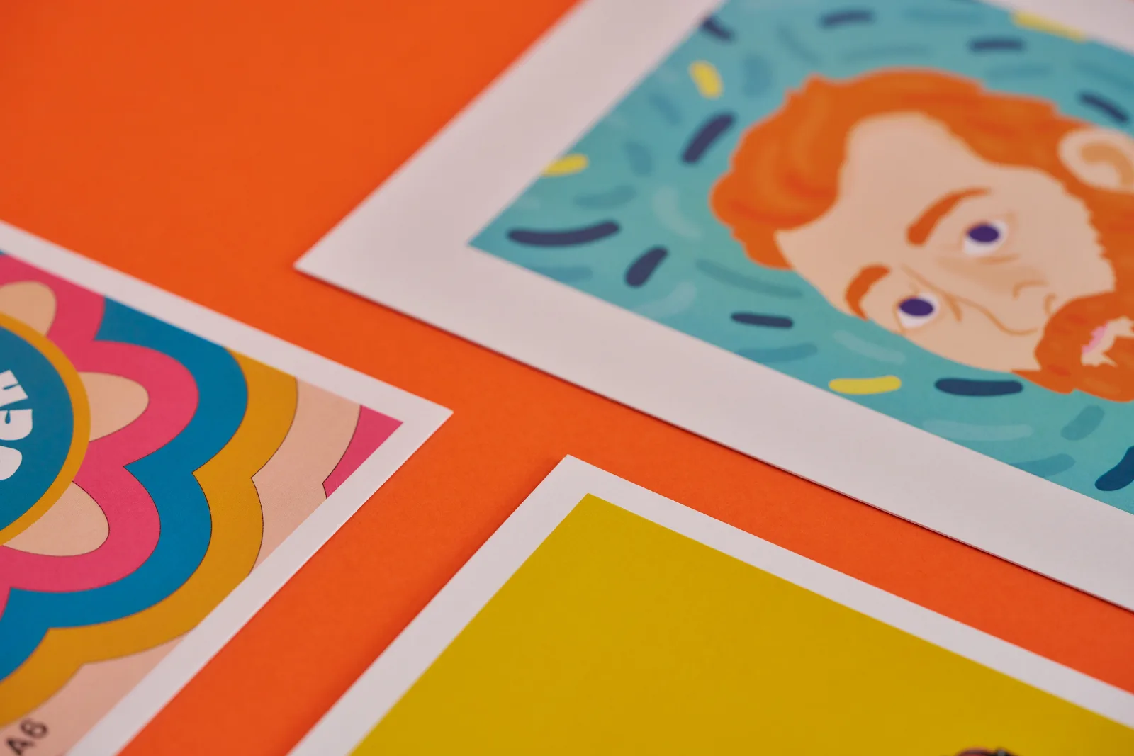 close up of 3 printed flyers with a colourful pattern, solid yellow and illustration of a bearded man on a bright orange background