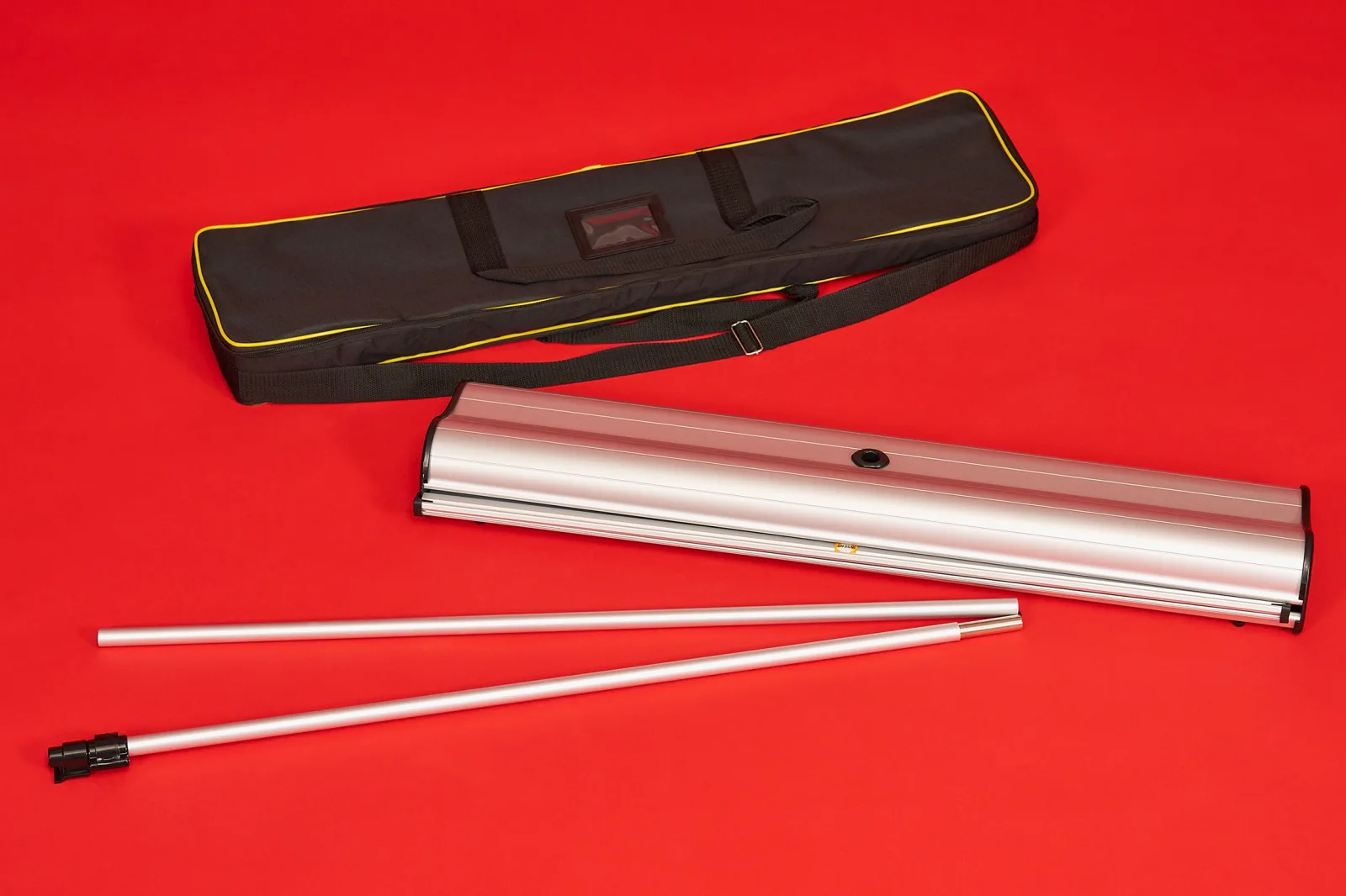 components of a premium roller banner including black and yellow carry bag, silver cassette and telescopic support pole