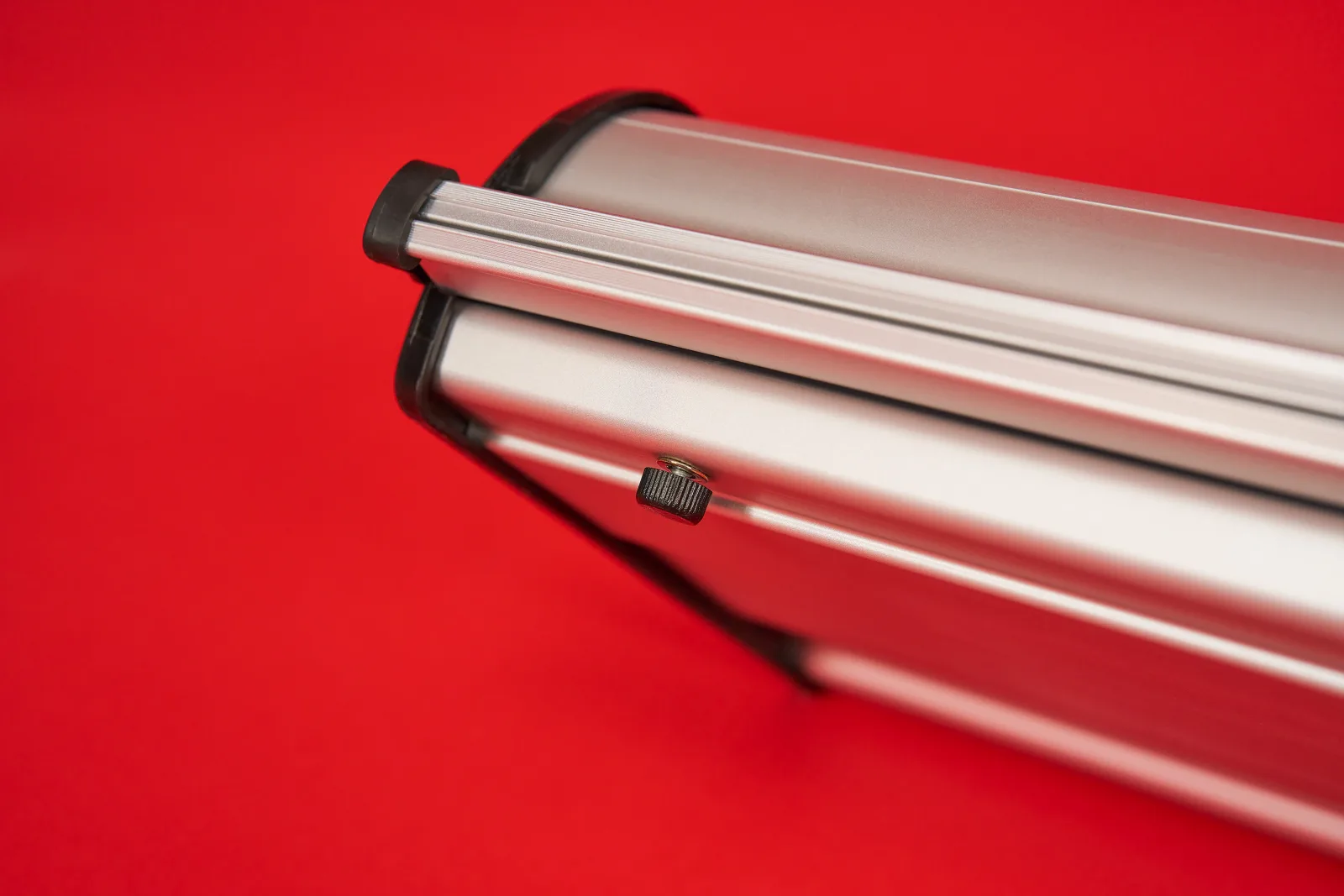 detail of the bottom of a silver premium roller banner cassette showing the adjustable height adjuster foot on a bright red background