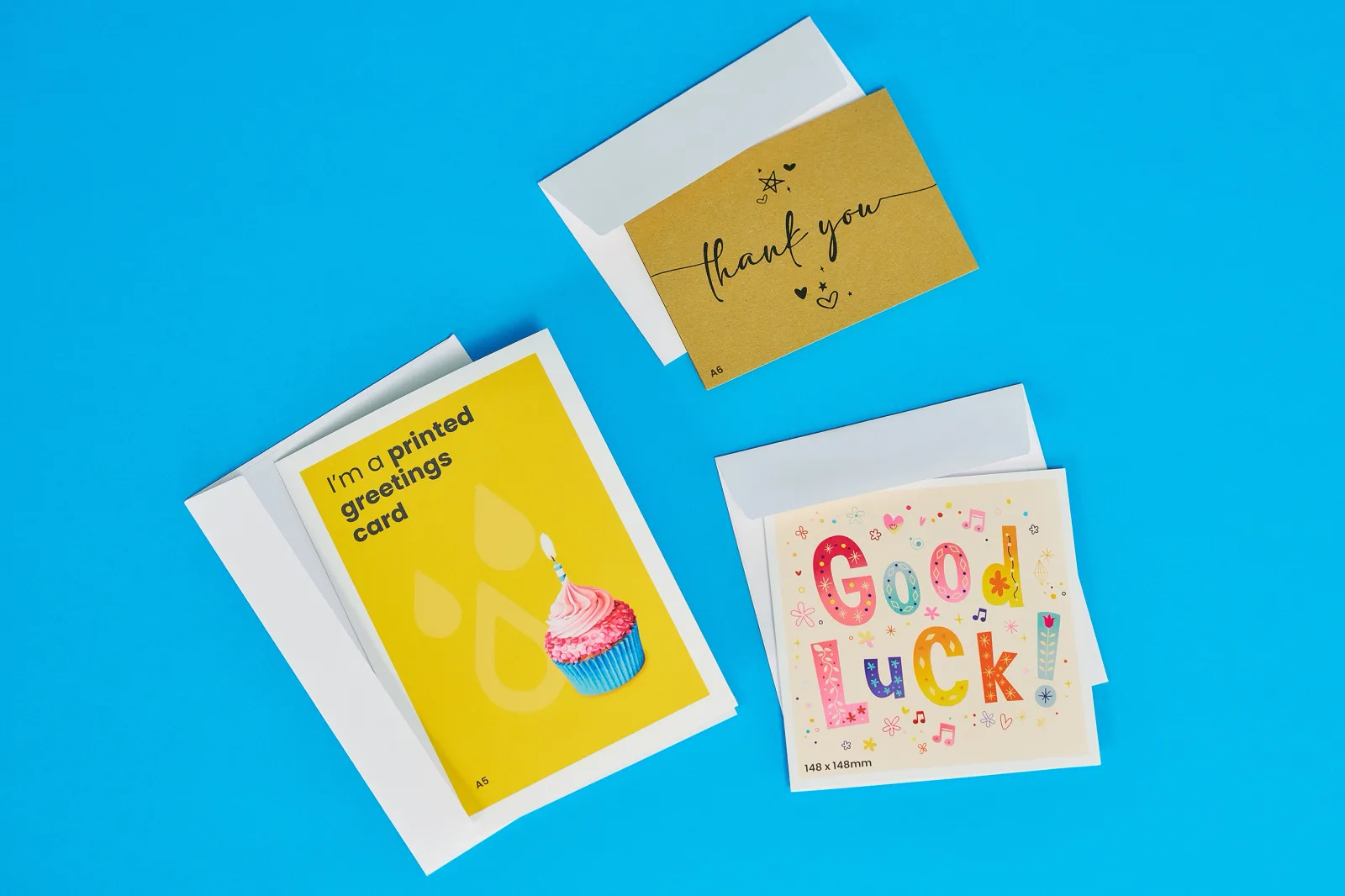greeting cards lying flat with envelopes with text 'i'm a printed greetings card', 'thank you' and 'good luck on a bright blue background