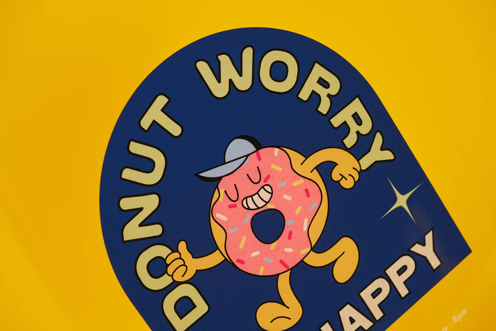 clear reverse vinyl window sticker printed in blue with a doughnut character illustration with text 'donut worry happy' on a bright yellow background