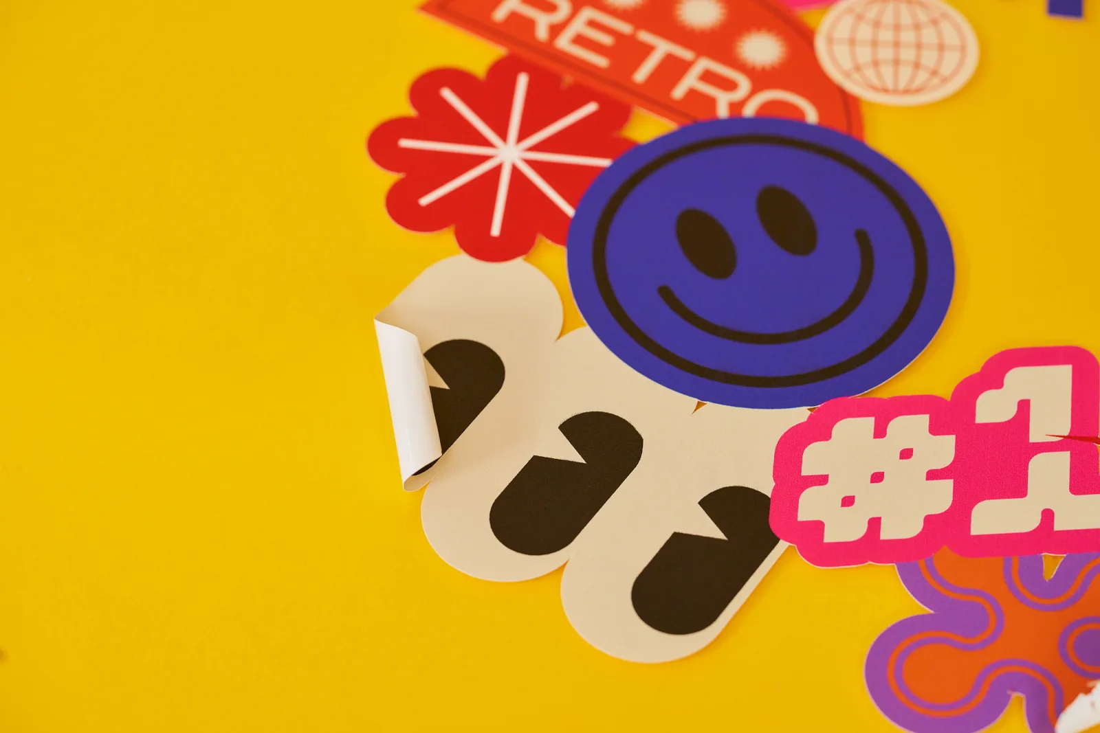 close up of a cluster of forward printed vinyl window stickers with smiley face text 'retro, #1' 3 eyes with the corner peeled over on a bright yellow background